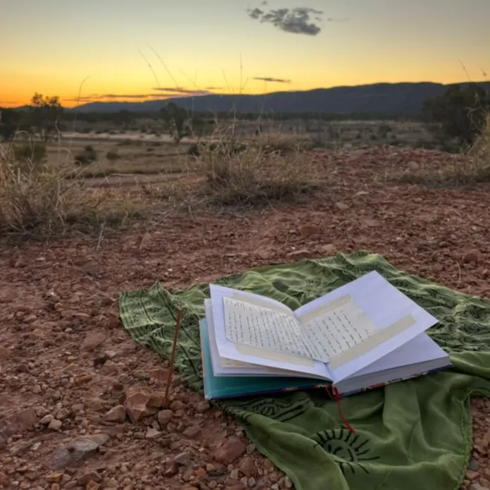 An open journal resting on a green cloth on red earth at sunset
