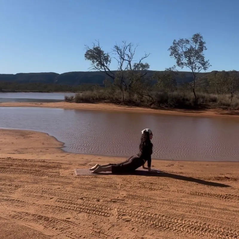 Liana in an upward-facing stretch on a sandy riverbank under a clear blue sky