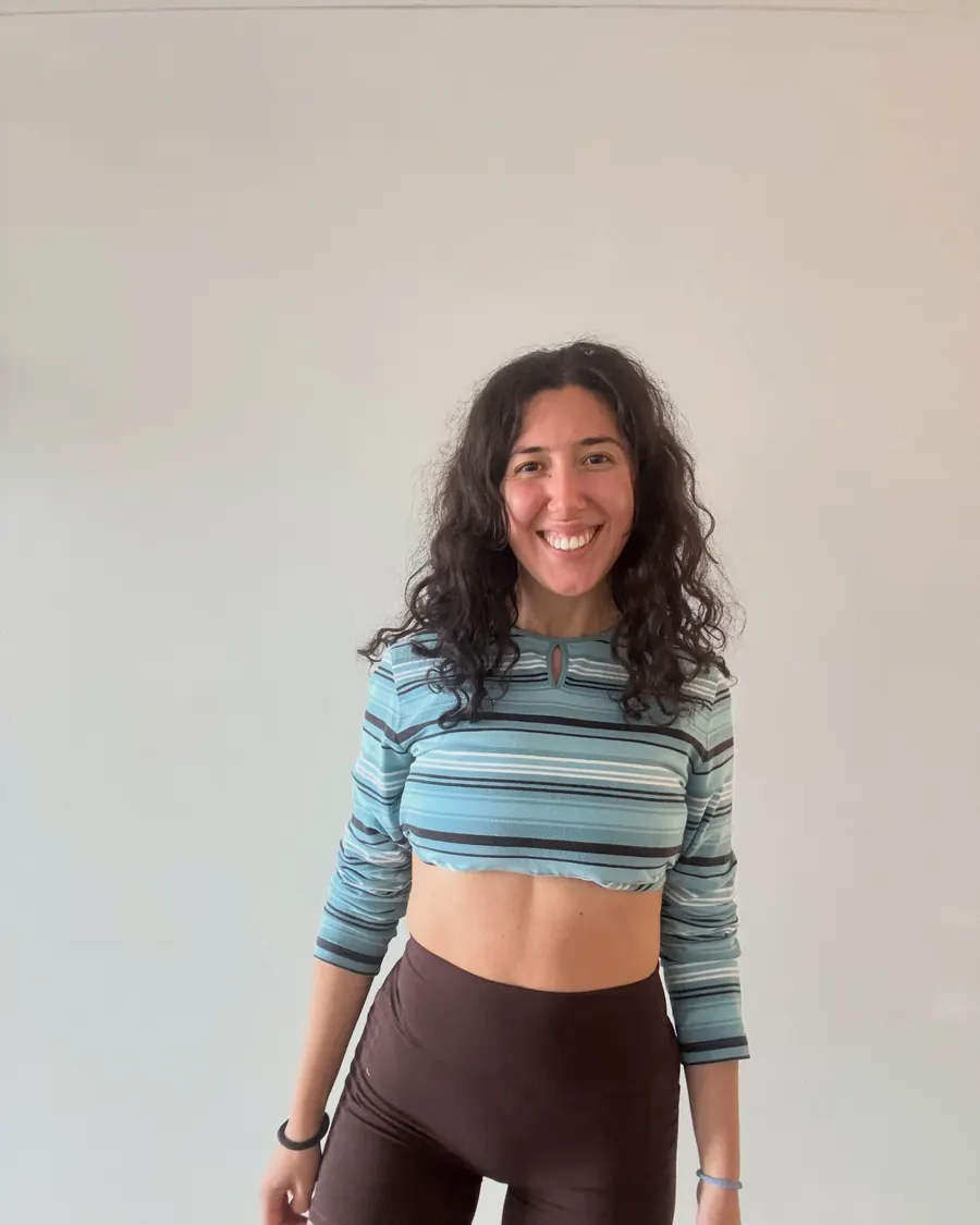 Liana smiling in a striped top against a pale wall