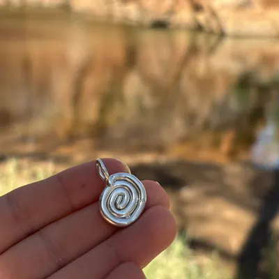 A handmade sterling silver spiral pendant held up to the light
