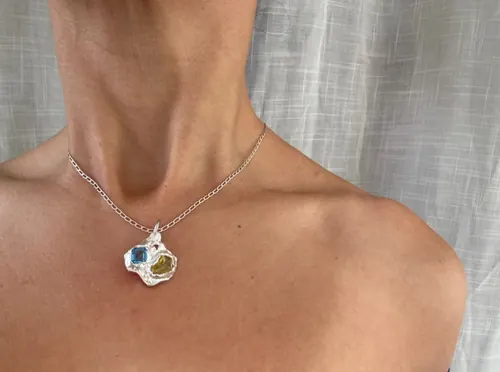 A silver spiral pendant with stones worn on a fine chain