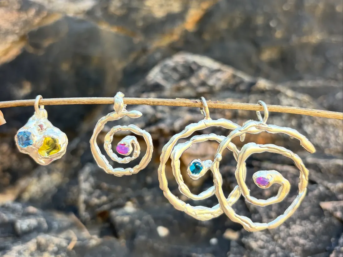 Silver spirals with blue, purple and yellow stones hanging on a wire over dark rock