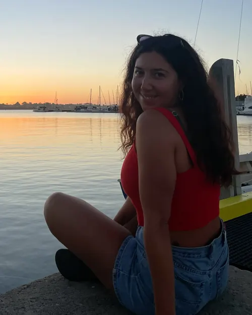 Liana sitting by the water at sunset, smiling back over her shoulder